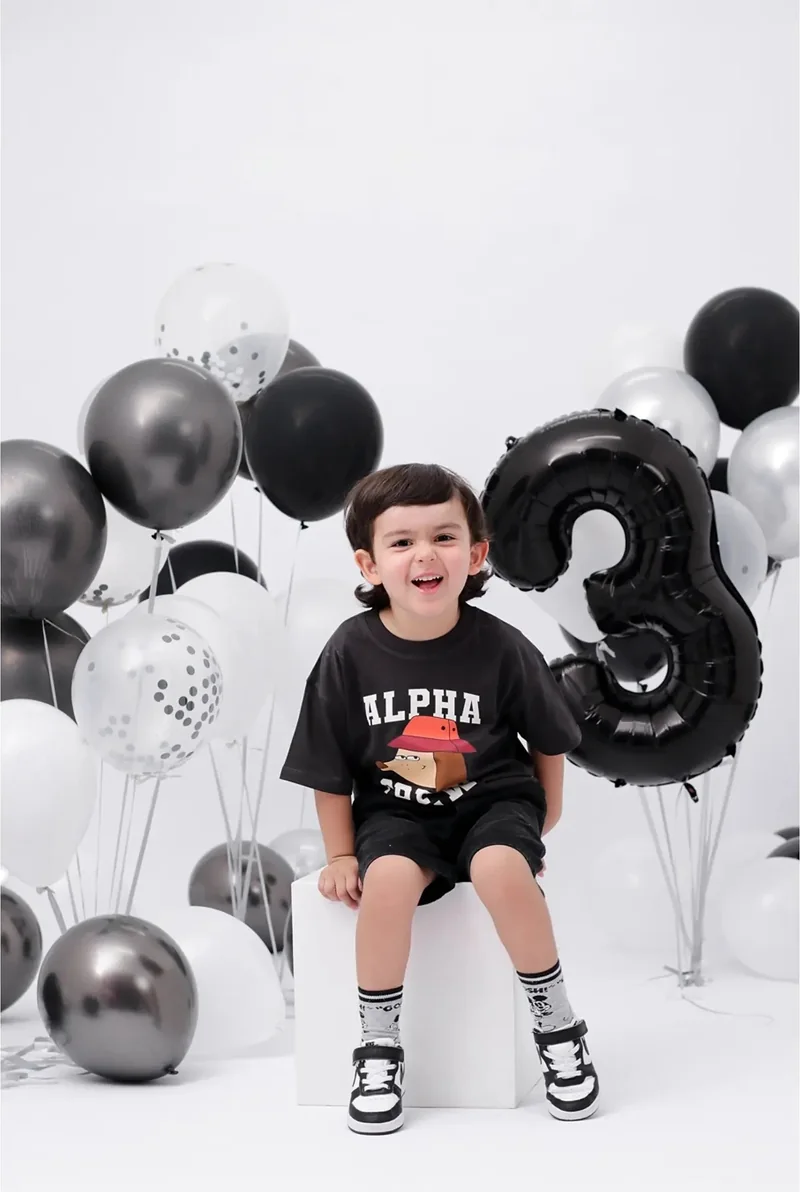 Niño sentado entre globos negros y plateados con el número tres