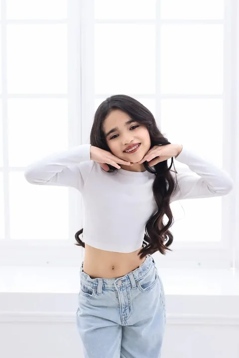 Niña sonriendo con las manos en la cara, en un estudio luminoso