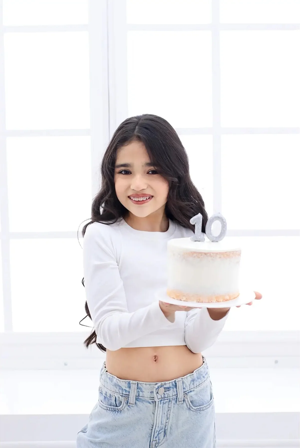 Niña sonriente con una torta de cumpleaños en un estudio blanco