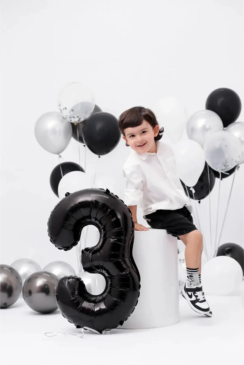 Niño junto a un globo negro del número tres