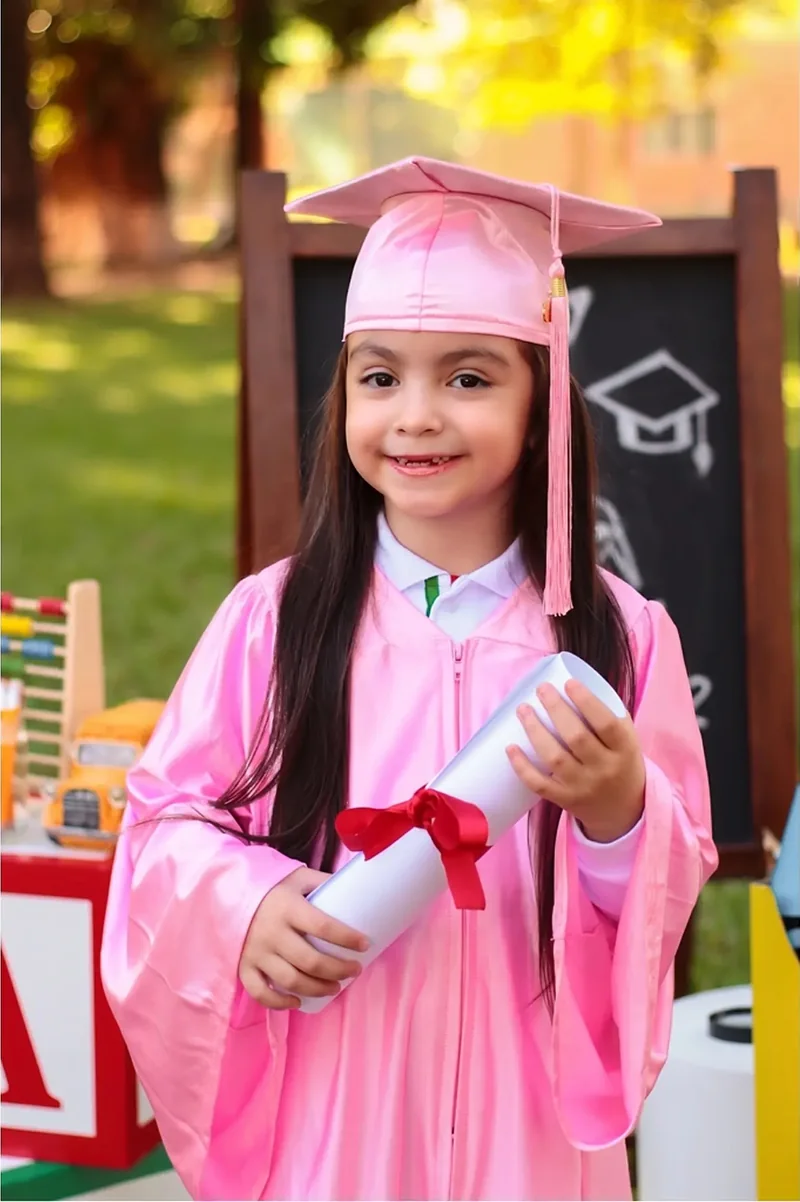 Niña con toga y birrete rosados sosteniendo su diploma