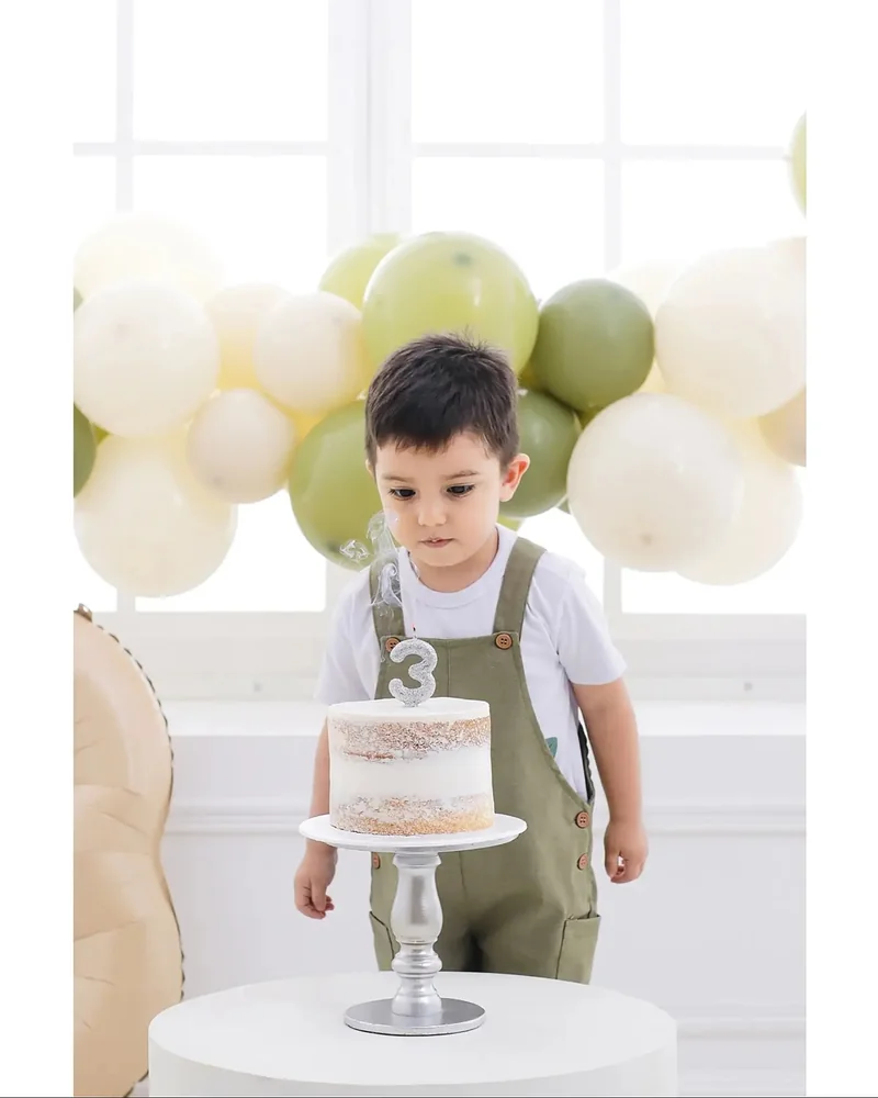 Niño con una torta de cumpleaños entre globos verdes y blancos