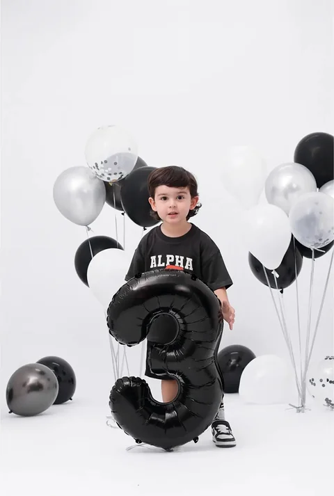 Niño sentado con un globo negro del número tres