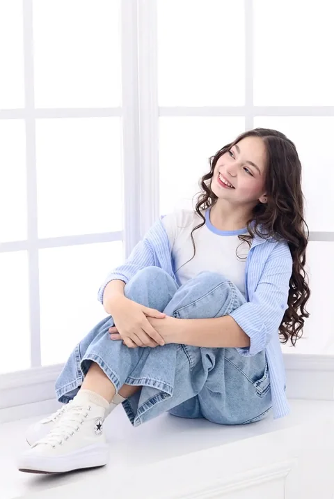 Niña sentada abrazando sus rodillas en un estudio blanco