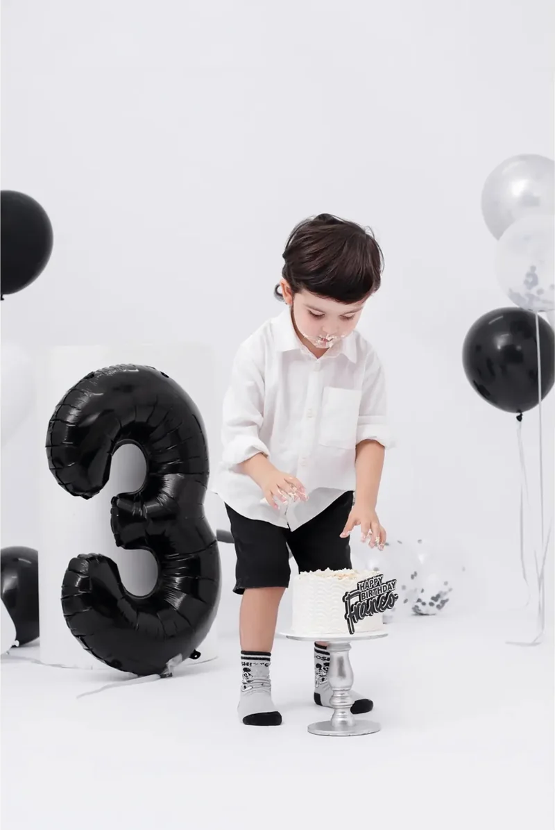 Niño de camisa blanca entre globos negros